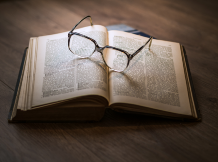 A brown-rimmed pair of glasses sit on top of a thick, open book.